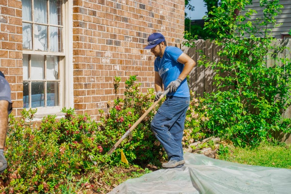 man raking soil in flower bed near house