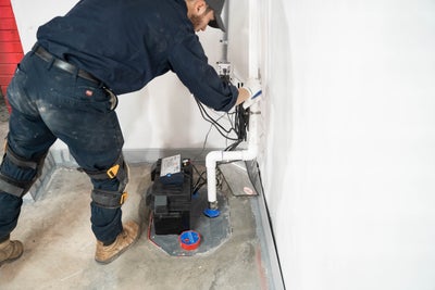 crew member installing a basement sump pump with a backup battery