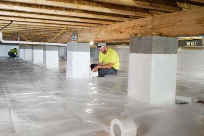 Crewmen installing a vapor barrier in a crawl space.