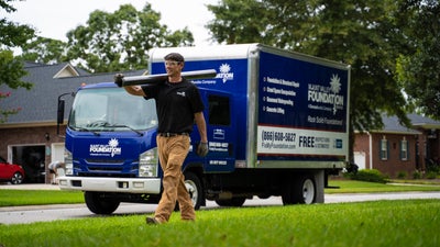 Mount Valley Foundation Services crew member holding a section of a push pier and walking past a company truck