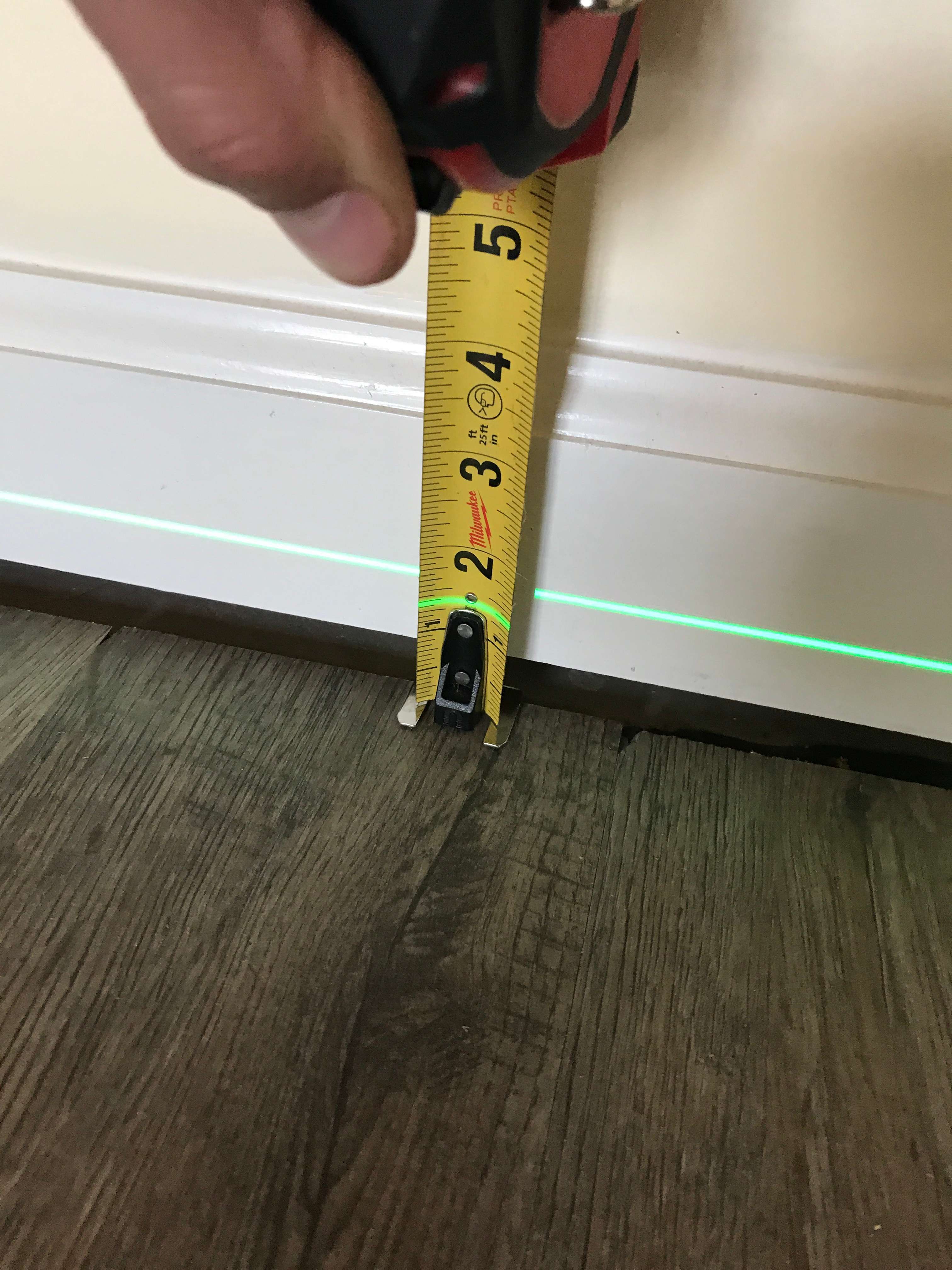 Close-up of a partially installed door, slightly ajar, with a visible green laser line on the hardwood floor—perfect for aligning steps if you're wondering how to fix sagging floors.