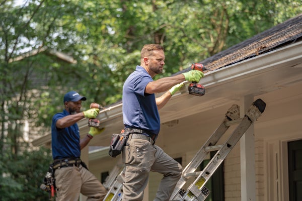 two Groundworks rew installing exterior gutter on house
