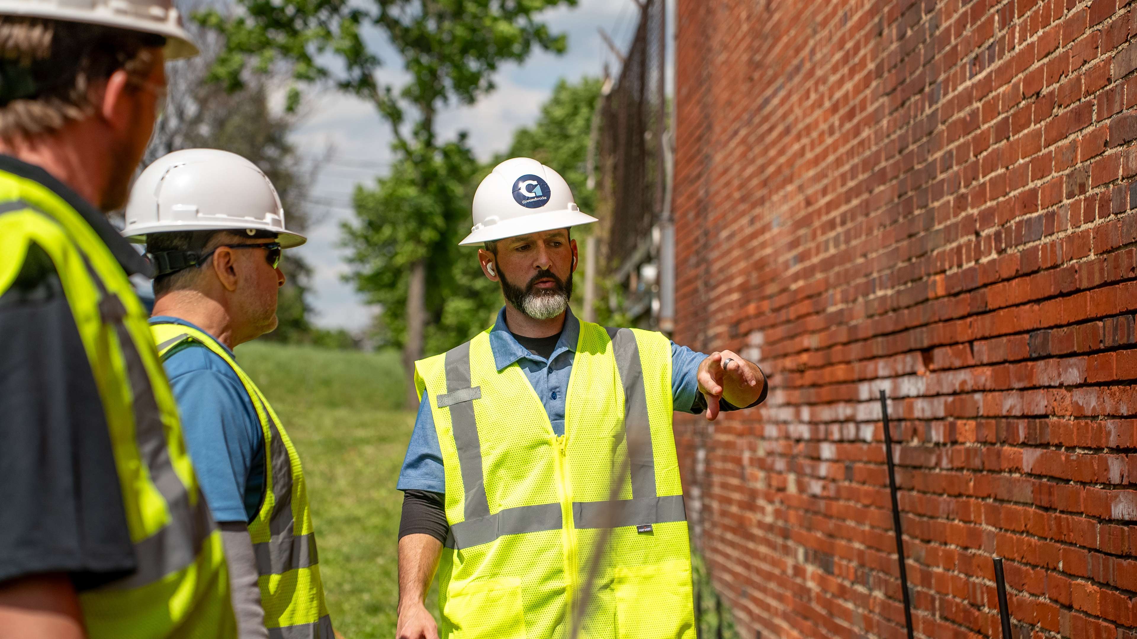 man in a hard hat points out damage to the side of a brick building