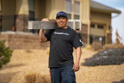 Smiling worker in Groundworks uniform holding a beam, standing in front of a house