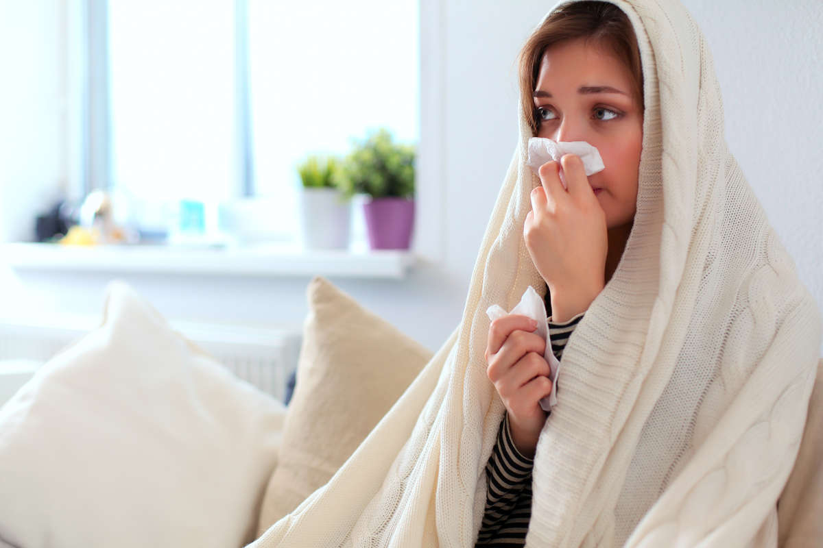 sick woman with blanket sneezing into tissue