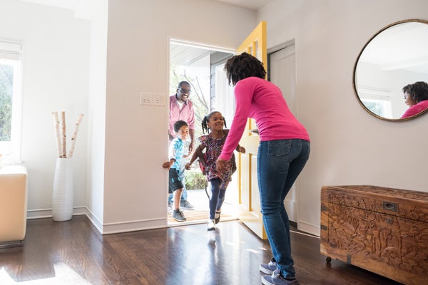 two children and father walking through front door of house greeted by the mother