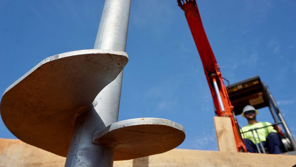 closeup of helical pier with crew member and heavy machinery