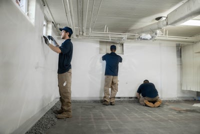 crew members installing basement wall vapor barrier and interior drains