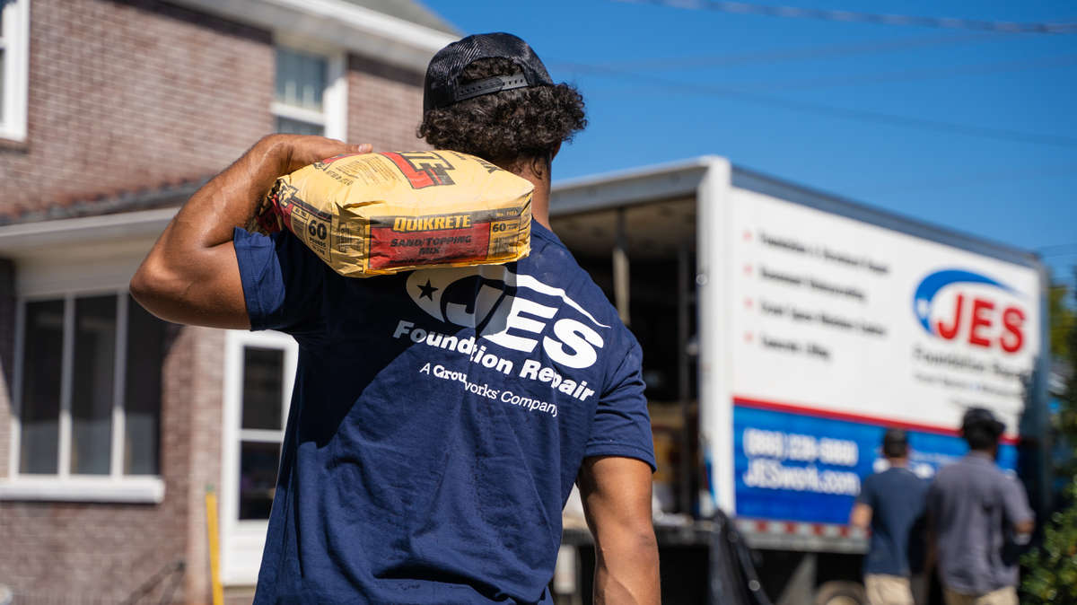 JES installer carrying materials to a truck in the background. Logo visible on back.