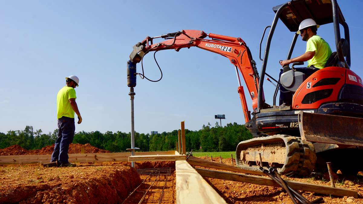two crew members installing helical piers with heavy machinery