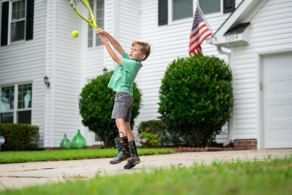 boy playing tennis on concrete driveway