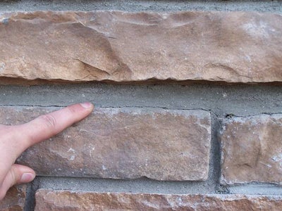 person pointing to hairline crack in exterior wall