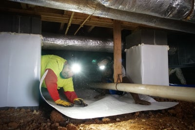 Man installing vapor barrier in a crawl space.