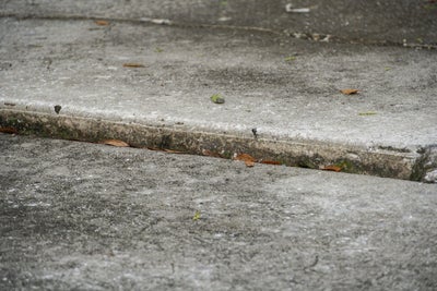 Close-up of a cracked and uneven concrete surface, indicating potential ground movement.