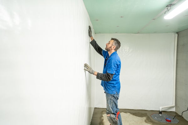 Groundworks crew installing basement vapor barrier to wall