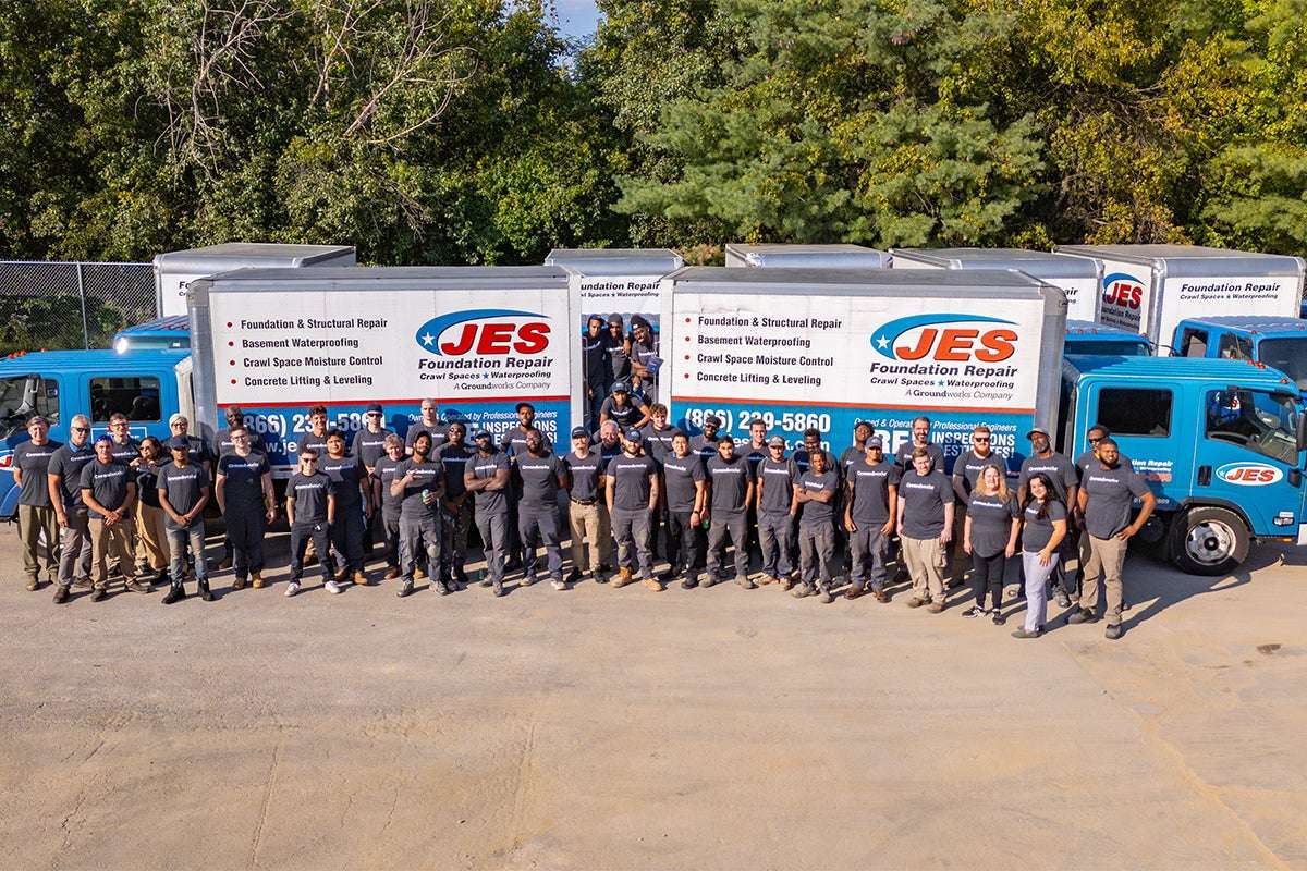 JES Foundation Repair crew standing in front of two work trucks and building