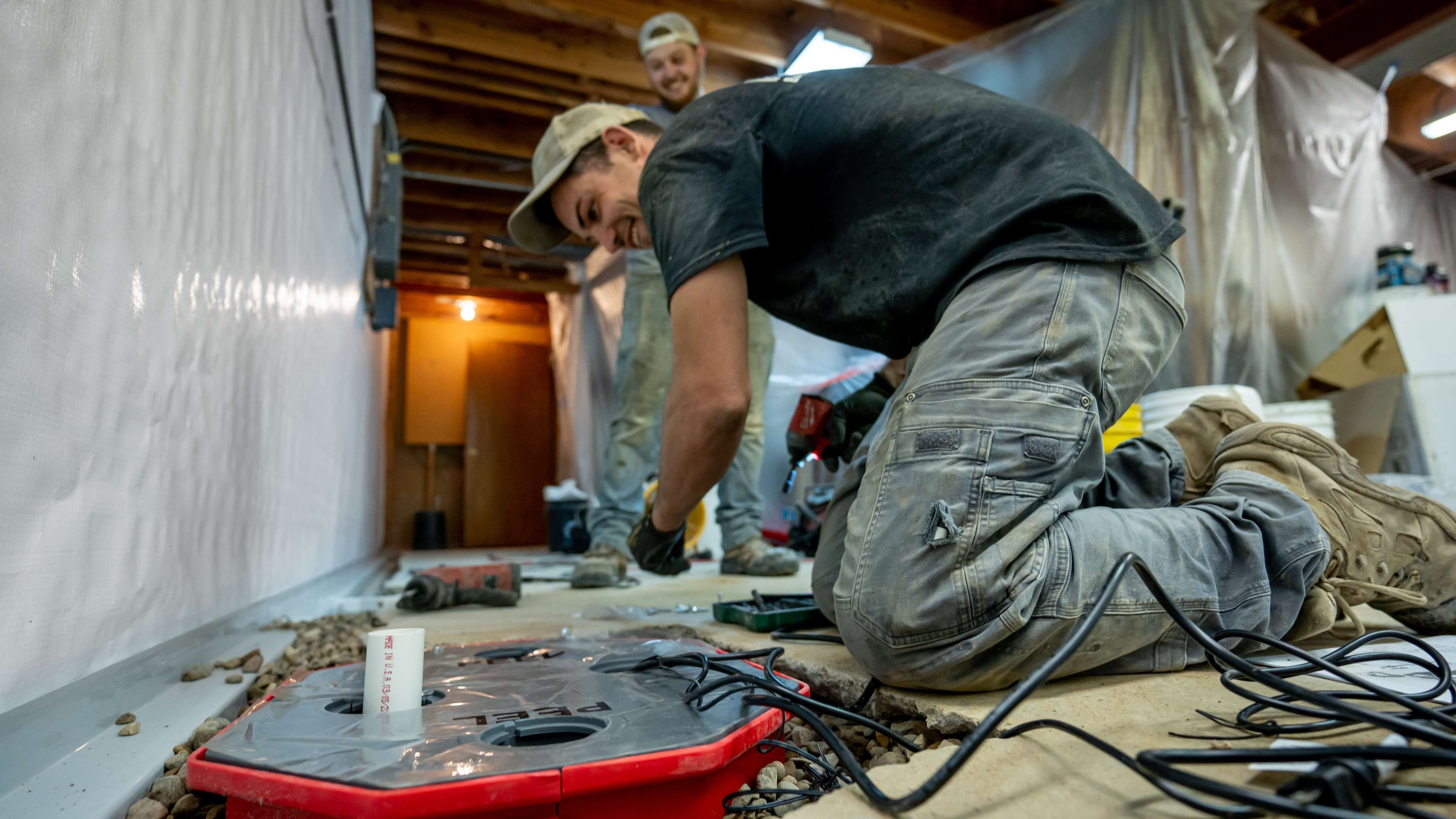 crew members install interior drainage and a sump pump in a basement
