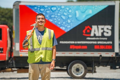 smiling AFS crew member holding a shovel on his shoulder and standing in front of a company truck