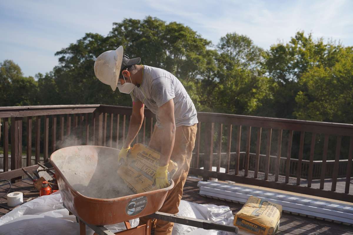 crew member pouring dry concrete into wheelbarrow