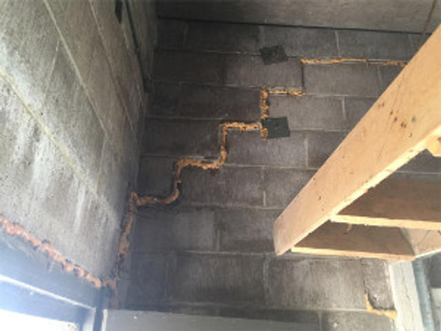 Concrete block wall with expanding foam sealant in zigzag pattern and a wooden shelf on the right.
