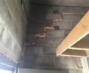 Concrete block wall with expanding foam sealant in zigzag pattern and a wooden shelf on the right.