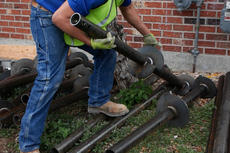 Crew picking up helical pier next to brick foundation wall.