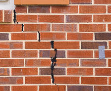 Brick wall with a vertical crack, partially sealed, hinting at the need to repair or replace the foundation; a small patch of gray tape on the right side.