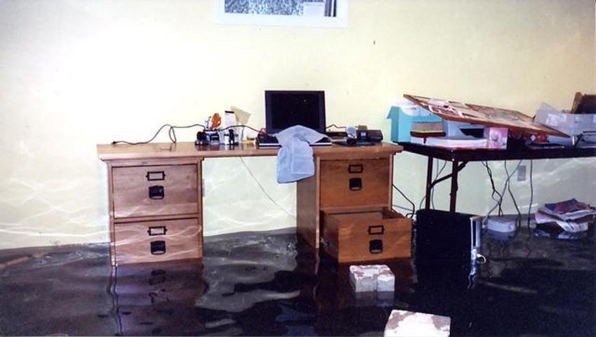 A flooded room with a wooden desk and a table, both partly submerged in water.