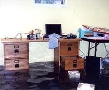 A flooded room with a wooden desk and a table, both partly submerged in water.