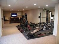 Home gym with various exercise equipment, mirrored wall, and nearby seating area with a large TV screen.