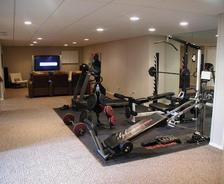 Home gym with various exercise equipment, mirrored wall, and nearby seating area with a large TV screen.