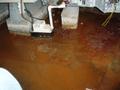 Flooded basement floor with waterlogged electrical equipment and wires.