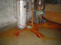 Water heater leaking rusty water onto a basement floor.