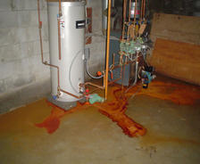Water heater leaking rusty water onto a basement floor.