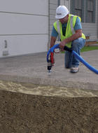 A worker in safety gear and helmet expertly injects material under a concrete slab using a hose and drill, skillfully performing essential concrete porch repair tasks.