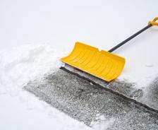 Yellow shovel outside with snow covering the uneven driveway.