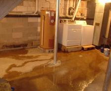Basement with water heater, washer, dryer, and water pooling on cement floor.