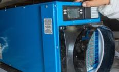 Person adjusting a blue dehumidifier unit in a crawl space.