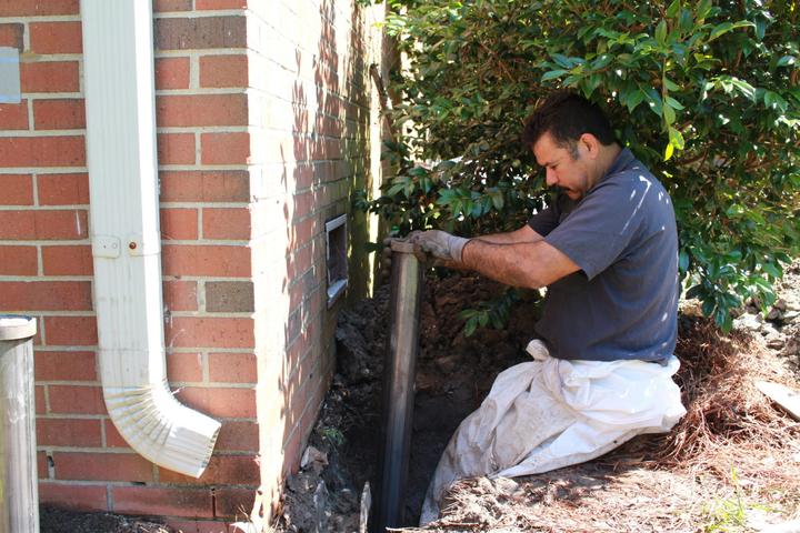The production crew installing a push pier inside the ground hole against the brick foundation.