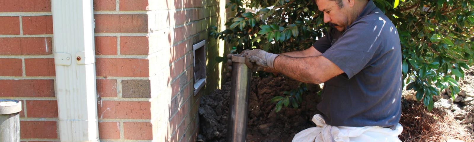 The production crew installing a push pier inside the ground hole against the brick foundation.