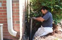 The production crew installing a push pier inside the ground hole against the brick foundation.