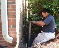 The production crew installing a push pier inside the ground hole against the brick foundation.