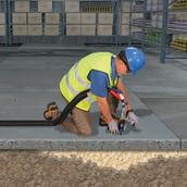 Worker in safety gear applies insulation foam underneath concrete flooring in a building under construction.