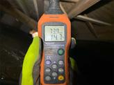 A digital humidity and temperature meter displaying 73.9% RH and 14.7°C is held by a person in gloves.