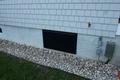 House exterior with gray siding, a black access panel, and a bed of white stones along the foundation.