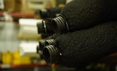 Close-up of black coiled hoses in a warehouse, with shelves and boxes blurred in the background.