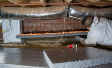 Person in protective gear installing insulation panels in a crawl space under a house.