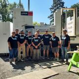 Group of people in matching T-shirts standing in front of a construction site under a clear blue sky.
