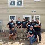 A group of people in work clothes poses in front of a house under construction.