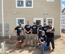 A group of people in work clothes poses in front of a house under construction.